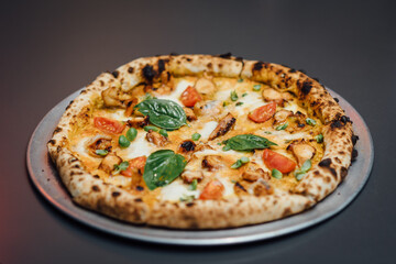 Napolitan pizza with sous-vide octopus, sautéed shrimp, basil, cherry tomatoes, mozzarella, and pesto sauce on a crispy wood-fired crust. Captured close-up, on modern gray minimalistic background