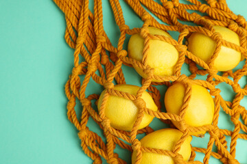 Macrame shopping bag with lemons on turquoise background, top view. Space for text
