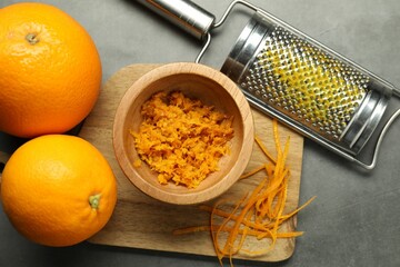 Orange zest, grater and fresh fruits on gray textured table, flat lay