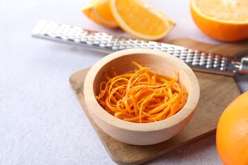 Fresh orange zest in bowl, fruits and grater on light textured table, closeup