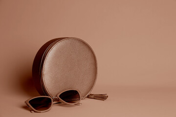 Stylish women's bag in mocha mousse shade and sunglasses on dark beige background. Trendy color of...