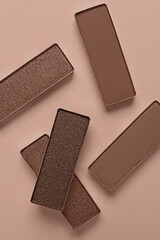 Eyeshadows in mocha mousse shades on dark beige background, top view. Trendy color of 2025 year