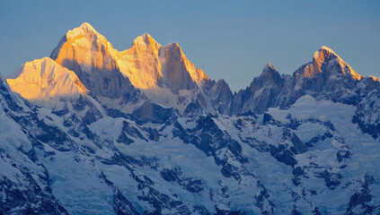 Obraz premium Golden Hour Peaks: A breathtaking panoramic view of majestic snow-capped mountains bathed in the golden light of dawn. The rugged peaks stand tall, casting long shadows across the snow-covered slopes.