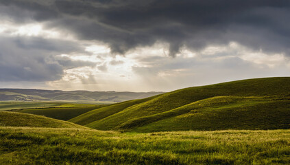 Dramatic Landscape: A breathtaking view of rolling hills bathed in the ethereal glow of sunlight breaking through dramatic, storm-laden clouds.