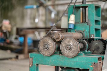 Close-up of a vintage green industrial machine with metal rollers and gears, used in a rustic Thai workshop environment.