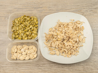 Peeled pumpkin seeds and peels in containers on a wooden table.
