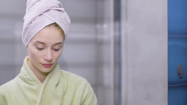 Beautiful young girl in bathrobe and towel on her hair. Holding makeup and thinking. Problematic skin care.