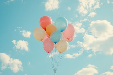 Pastel colored balloons floating against a blue sky with white clouds, celebrating a happy occasion