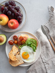 Healthy breakfast with whole wheat toast, avocado, fried egg, and fresh fruits