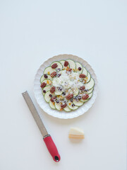 Zucchini carpaccio with parmesan, pecan nuts, raisins, and grater on white background