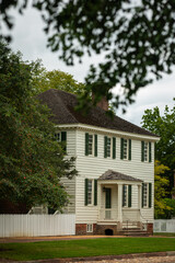 Vintage wooden House in Colonial Williamsburg Open Air Museum with green Lawn in Front on a Summer Day with cloudy Sky