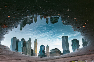 Fototapeta premium City skyline reflects in calm lake surrounded by trees during sunset with vibrant clouds and soft glow