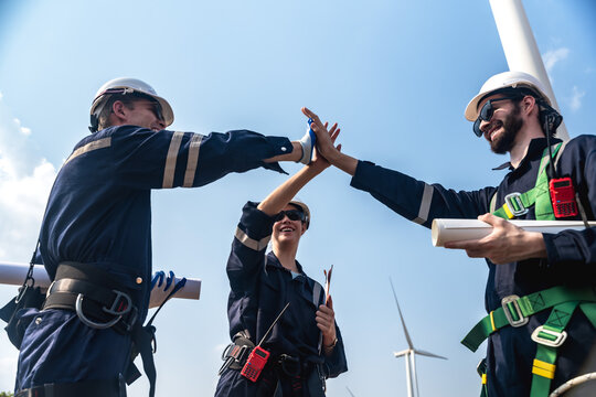 Group of professional males and female wind turbine engineers putting hands together after finish working in wind power plant farm