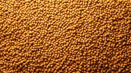 Close-up view of numerous small, uniformly-sized, golden-brown pellets forming a dense textured...