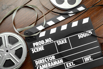 Movie clapper and film reels on wooden table, flat lay