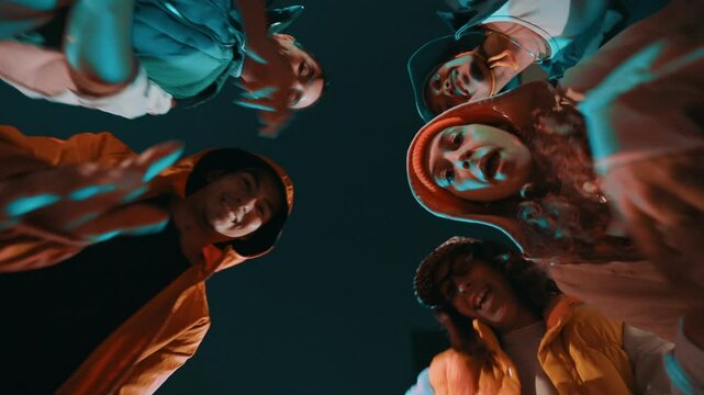 Group of young trendy friends looking down on a circle, moving, dancing and having fun at night