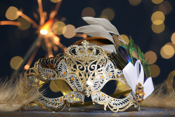 Fototapeta premium Beautiful carnival mask and confetti on table against dark background with blurred lights, closeup