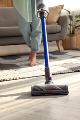 Woman cleaning floor with cordless vacuum cleaner at home, closeup