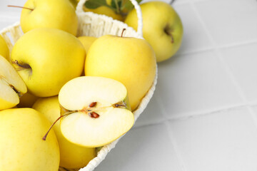 Fresh ripe yellow apples in basket on white tiled table, closeup. Space for text