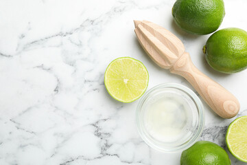 Wooden juicer and fresh limes on white marble table, flat lay. Space for text