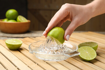 Woman squeezing juice of fresh lime with juicer at wooden table, closeup