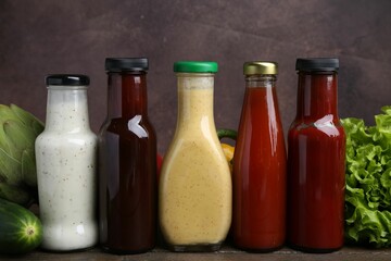 Tasty sauces in glass bottles and fresh products on wooden table, closeup