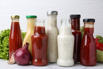 Tasty sauces in glass bottles and fresh products on white marble table, closeup