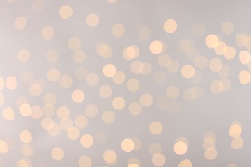 Blurred view of golden lights on light background, bokeh effect