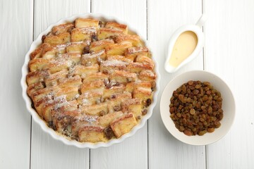 Delicious bread pudding with raisins, powdered sugar, condensed milk on white wooden table, flat lay