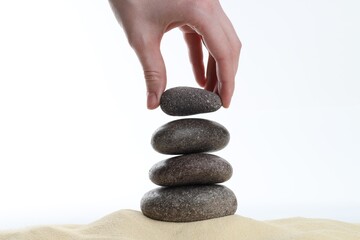 Woman making stack of stones on white background, closeup. Harmony and life balance