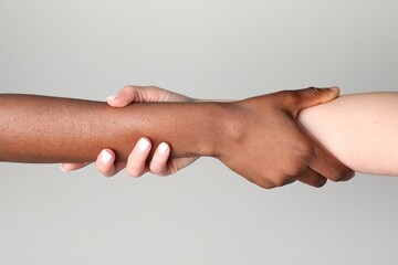 Stop racism. People of different skin colors holding hands on light grey background, closeup