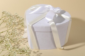 Beautiful wedding gift and gypsophila flowers on beige background, closeup