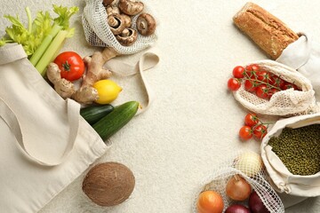 Eco bags with different food products on white textured table, flat lay. Space for text