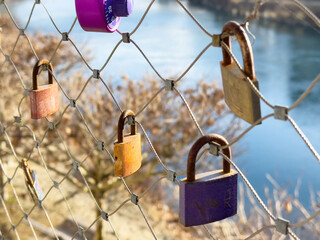 Love locks attached to a metal fence overlooking a river on a sunny day