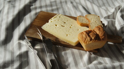 Sweet Asiago cheese, fresh cheese from cow's milk alpine 40 days aged, with fresh sliced ​​white bread and natural butter, peasant table, white striped tablecloth, on a wooden board, Italy