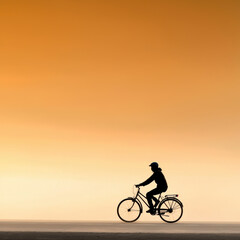 Obraz premium silhouette of man riding bicycle against warm orange sunset sky, evoking sense of freedom and tranquility
