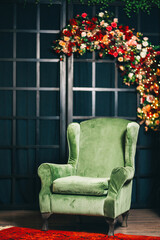 green armchair against of a black lattice decorated with flowers. photo zone with a soft armchair