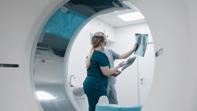 Senior doctor and assistant examining a tomographic lungs scan. Doctor examining X-ray, Magnetic resonance image in front of MRI, CT scanner background. Medical research ads, Health Care concept