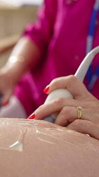 Pregnant woman doing ultrasound in clinic. Examination of baby at ultrasound. Doctor performing sonogram on belly in clinic. Process of fetus ultrasonography. Close-up. Vertical video