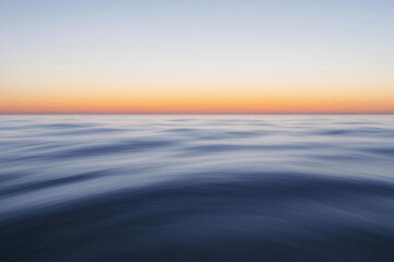Obraz premium Sunset over calm ocean waters creates a serene atmosphere with vibrant colors on the horizon