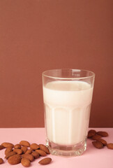Fresh almond milk in glass and almonds on brown background. Healthy vegan plant based alternative milk replacer. Space for text