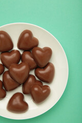 Red chocolate sweets as heart on plate on mint background. Valentine's day concept.