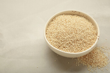 Raw sesame seeds in white bowl on light background.