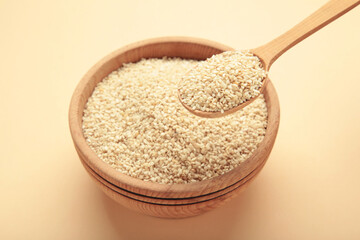 Raw sesame seeds in wooden bowl and spoon on beige background.