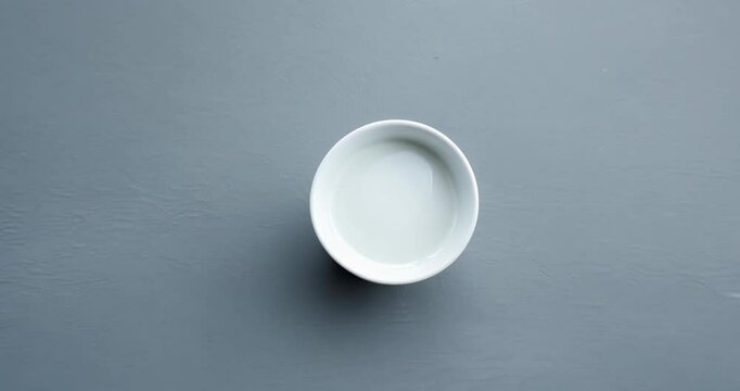 A white coffee cup resting on a flat grey surface, filmed with a slow zoom-out to show the contrast between the cup's clean lines and the minimalist background.