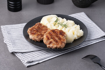 Savory grilled patties with creamy mashed potatoes and fresh rosemary on a dark plate