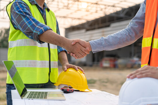 Engineer team building, teamwork contractor asian young man partnership, builder agreement handshake plan home project contract at construction site .Happy architect, surveyor worker shaking hands.