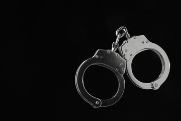 Metal chain handcuffs on black background, closeup. Space for text