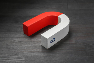 One horseshoe magnet on black wooden table, closeup