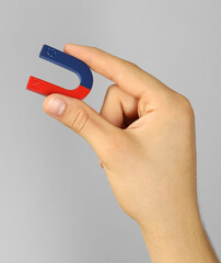 Man holding horseshoe magnet on grey background, closeup